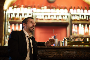 Portrait of handsome mature man drinking whiskey sitting at bar counter in luxury restaurant, copy space