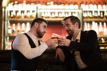 Side view portrait of two successful business people drinking whiskey at bar counter celebrating successful deal after work