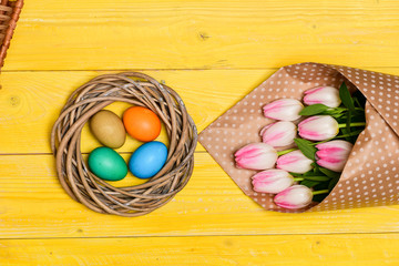 Spring vibes. Colorful bright eggs and bouquet fresh tulip flowers on yellow background top view. Spring holiday. Tradition celebrate easter. Happy easter season. Easter eggs symbol. Easter is coming