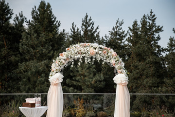 A flower arch with the peach curtains and a little table near it. Forest at the background.