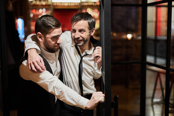Waist up portrait of waiter carrying drunk man out of bar at night, copy space