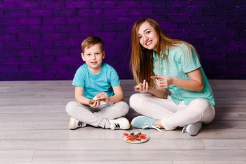 smiling young woman and boy in blue shirts sit on the floor