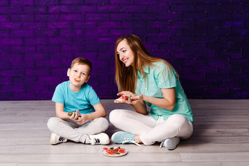 young long-haired mother and seven-year-old son in shirts and sneakers sitting on the floor and...