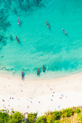 View from above, aerial view of a beautiful tropical beach with white sand and turquoise clear water, longtail boats and people sunbathing, Freedom beach, Phuket, Thailand.