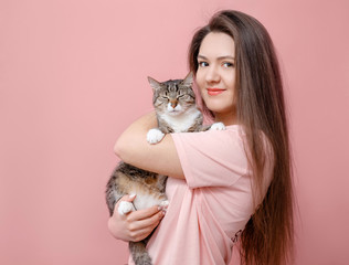 young attractive woman hugging cat in hands, pink background
