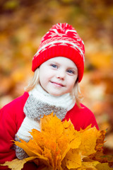 little girl 4 years old in a red hat and coat walking in autumn park in October, during the golden autumn with a bouquet of yellow maple leaves smiling