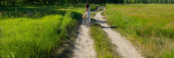 girl traveling by bike on a dirt road in the background of the forest in the evening.