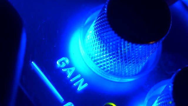 Extreme close-up turning button gain of control panel on amplifier sound with flashing blue light high angle. Hand touching tumblers or buttons for increasing music volume on amp macro shot