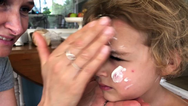 Mom applying sunscreen to her toddler son