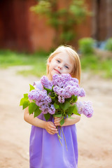 smiling little cute blonde girl with a bouquet of lilac in the hands in the lilac dress