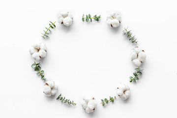 Flowers frame on white desk with fresh eucalyptus branches and cotton. Flat lay, top view, copy space