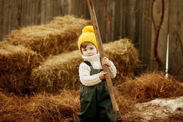 Small boy in yellow hat with shovel against the hay