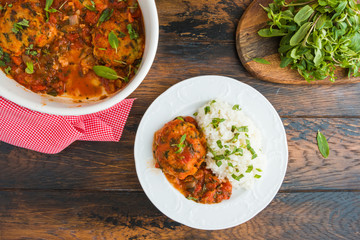 Fish rissoles  in spicy tomato sauce with fresh mint and boiled rice. White dish and plate on wooden rustic table, top view