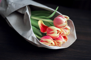 Fototapeta na wymiar Five roses in a peach-colored kraft paper on a dark wooden background, natural light, horizontal arrangement