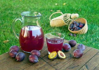 Prune juice in a decanter and a glass with ripe plums.