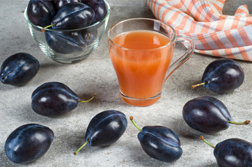 Blue plums and plum juice in a mug on a gray table.