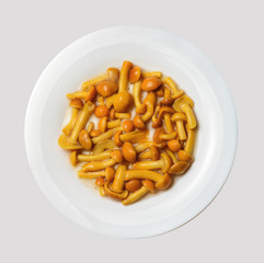 Marinated savory mushrooms on a white round plate. Light gray isolated background. View from above. Close-up.