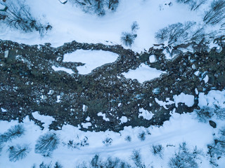 Aerial view of snow covered stones in river flowing through winter landscape from above.