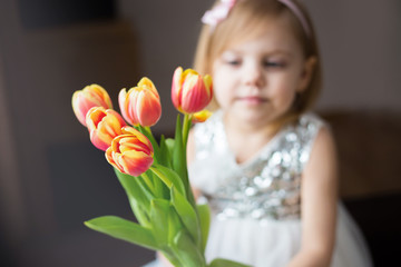 Obraz na płótnie Canvas cute little blonde girl of three years with peach tulips close-up, smiling, look at the flowers, horizontal photo, the girl is not in focus