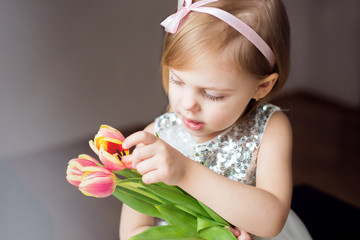 cute little blonde girl of three years with peach tulips close-up, smiling, look at the flowers, horizontal photo