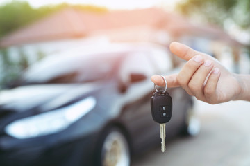 Business man hand holding car keys front with car on background. parking in front of the house....