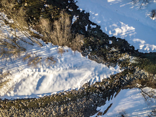 Aerial view of snow covered stones in river flowing through winter landscape from above. Island in...