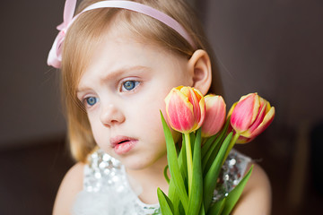 Obraz na płótnie Canvas cute little blonde girl of three years with peach tulips close-up, sad, side view, horizontal photo,