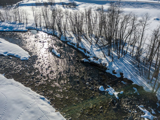 Aerial view of snow covered stones in river flowing through winter landscape from above.