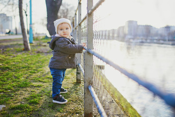 One year old girl standing next to metal fence in park