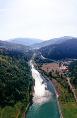 Aerial scenic view of a dam constructed on a beautiful valley in mountains. water storage reservoir. road with beautiful views for travel and holidays. lake Lzvorul Muntelui, Romania, vertical photo