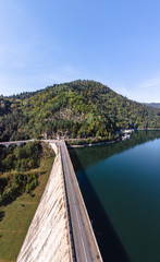 Aerial scenic view of a dam constructed on a beautiful valley in mountains. water storage reservoir. road with beautiful views for travel and holidays. lake Lzvorul Muntelui, Romania, vertical photo