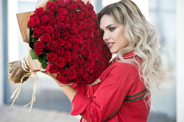 Elegant beautiful blonde woman is wearing green fashion dress in cafe holding with big bouquet of...