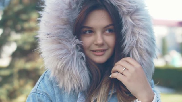 Portrait of nice young girl with jeans fur jacket in park. Close up 4k. Slow motion footage.