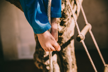 Bare feet of a boy holding on to a rope while climbing up it.