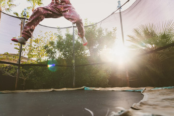 Little girl enjoying her vacation jumping on the trampoline doing acrobatic exercise outdoors.