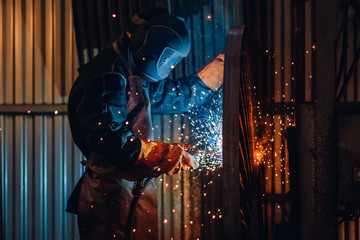 Professional welder performs welding work on metal in protective mask. Industrial worker concept