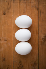 Three white eggs in a raw on a wood ground