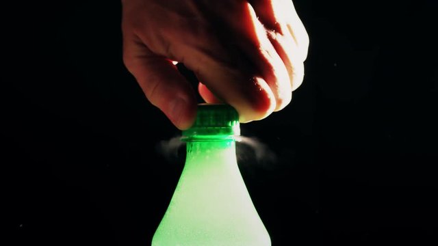 Man opens green plastic bottle of foamy soda against black background