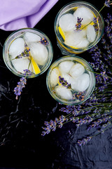 Fototapeta na wymiar Lavender lemonade with lemon and ice on black background.