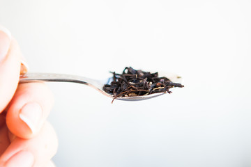 Black tea leaves in the spoon on a white ground