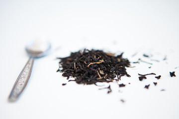 Black tea leaves and the spoon on a white ground 
