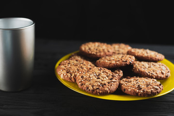 Oatmeal cookies with seeds and sesame seeds on a yellow plate, on a black wooden background