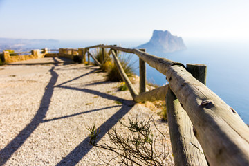 Wooden railing in a mountain path, the viewpoint of Morro de Toix, Penon of Ifach in Calpe is in the background