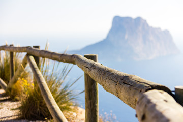 Fototapeta na wymiar Wooden railing in a mountain path, the viewpoint of Morro de Toix, Penon of Ifach in Calpe is in the background