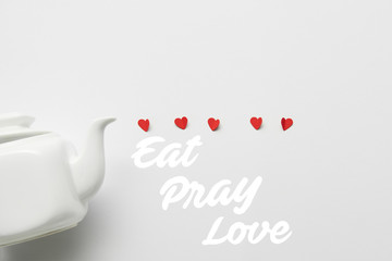 top view of tea pot and red paper cut hearts on white background with 