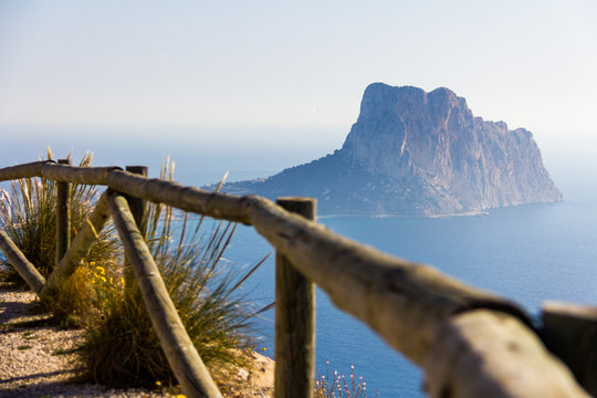 Wooden railing in a mountain path, the viewpoint of Morro de Toix, Penon of Ifach in Calpe is in the background