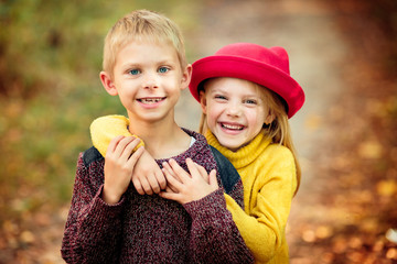 little cute happy girl, baby 6 years old in a red hat, yellow sweater is standing in a park or in...