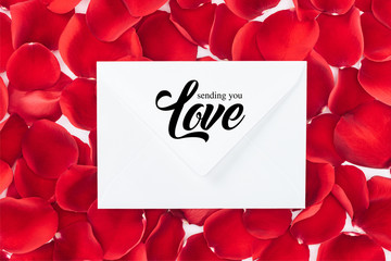 top view of envelope with "sending you love" lettering and red rose petals on background