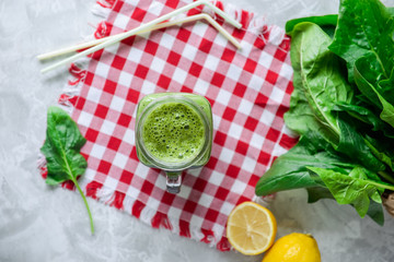 Fototapeta na wymiar Top view Healthy green spinach smoothie in a jar mug with ingredients on the checkered napkin on the white marble table. Selective focus.