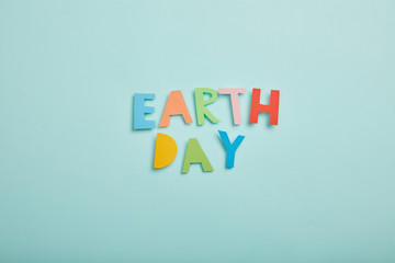 top view of colorful paper letters on turquoise background, earth day concept